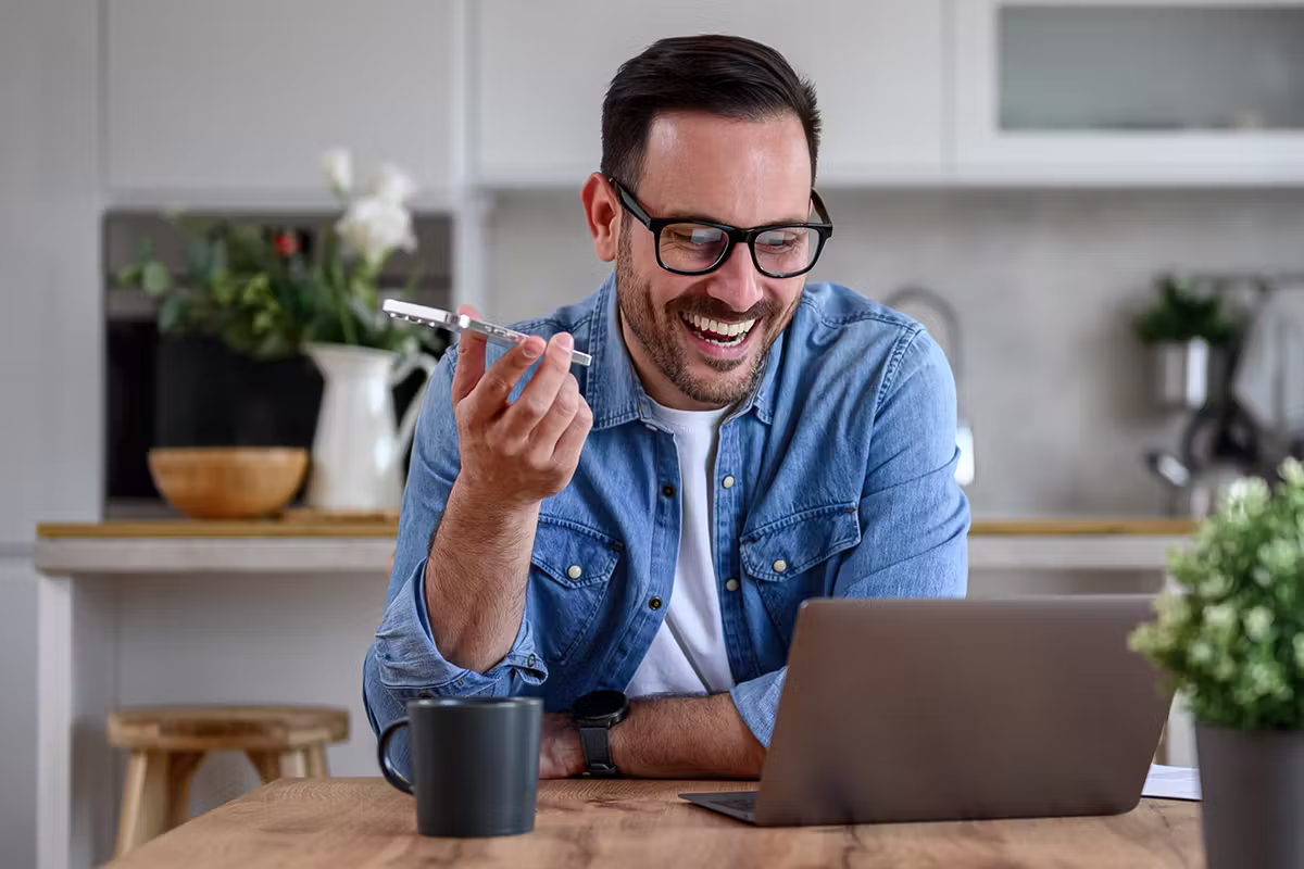 Business owner taking a call while working at a laptop in a bright kitchen